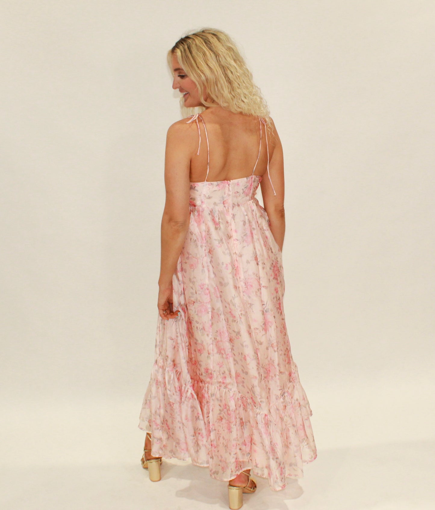 Back view of a flowy pink floral maxi dress with adjustable straps and ruffled hem.