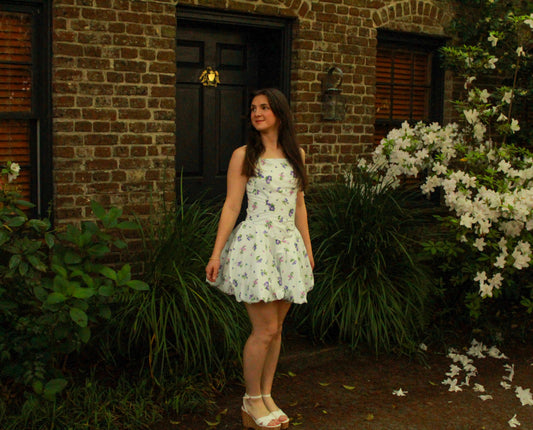 White floral sundress with a flared skirt, perfect for summer outings, worn by a model outdoors.