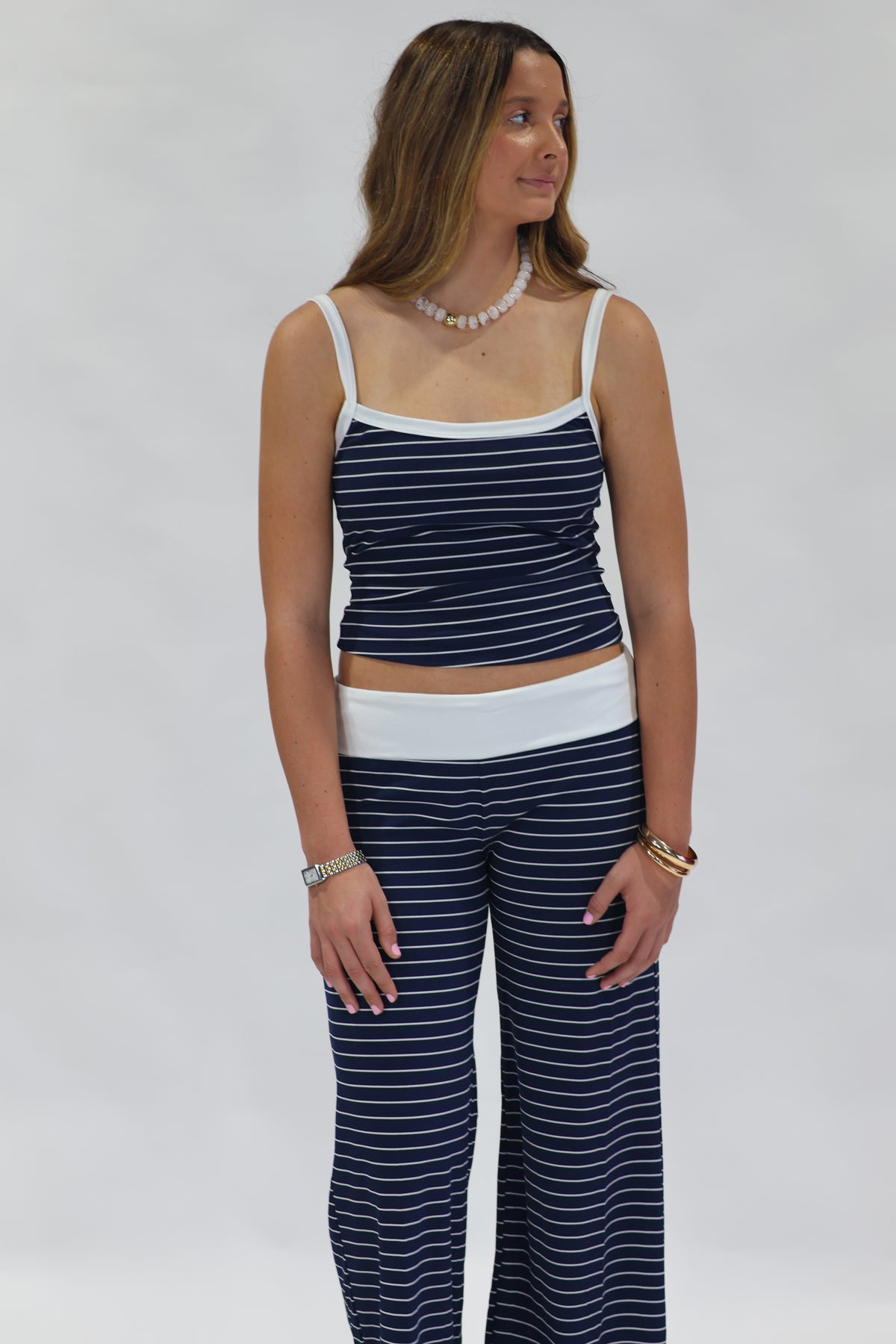 A woman modeling a matching two-piece loungewear set consisting of a navy blue and white striped camisole top and wide-leg pants, set against a plain light gray background.