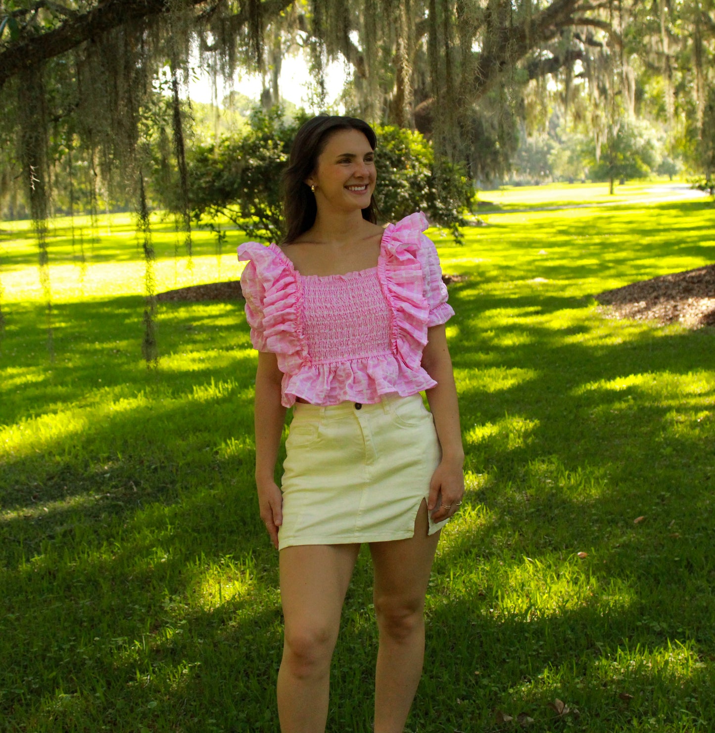 Smocked pink ruffled top paired with a white mini skirt in a sunny park setting.