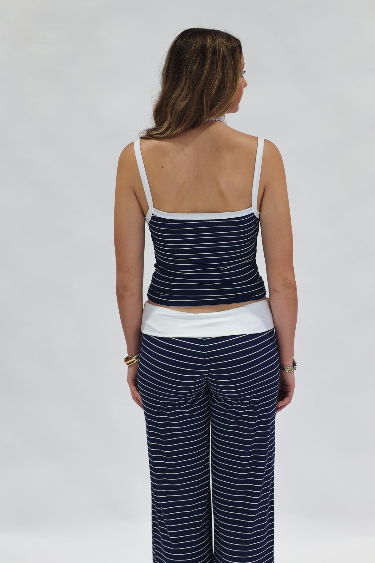 A woman shown from the back wearing a matching navy blue and white striped lounge set, consisting of a camisole top and wide-leg pants, against a plain light gray background.