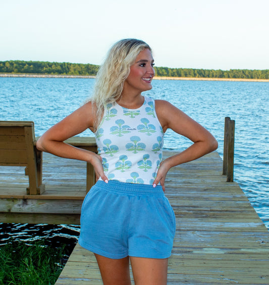 Woman standing on a dock by a lake wearing a sleeveless top and shorts.
