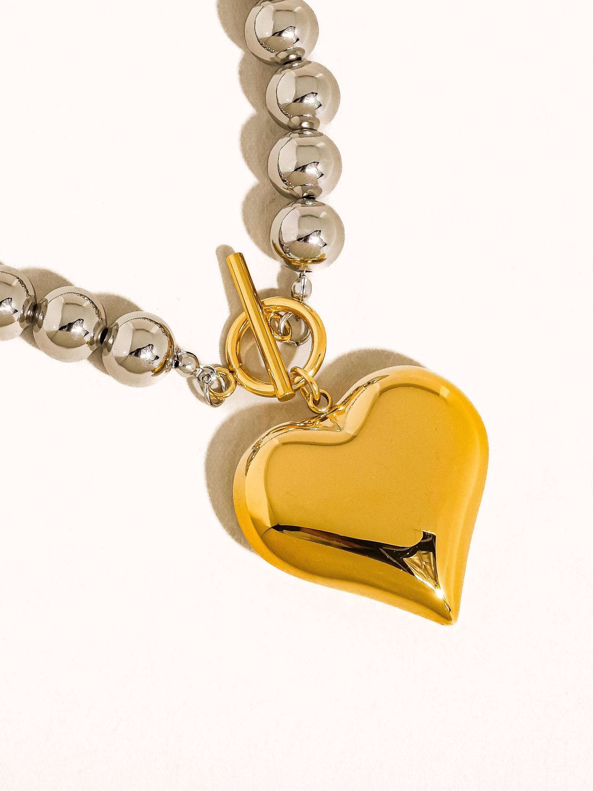 Gold heart pendant necklace with silver beads, features a toggle clasp for secure fastening.