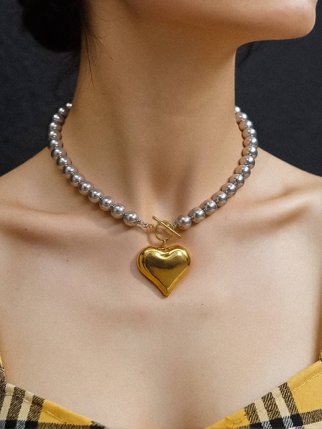 Elegant silver pearl necklace with a glossy gold heart pendant, perfect for chic outfits.