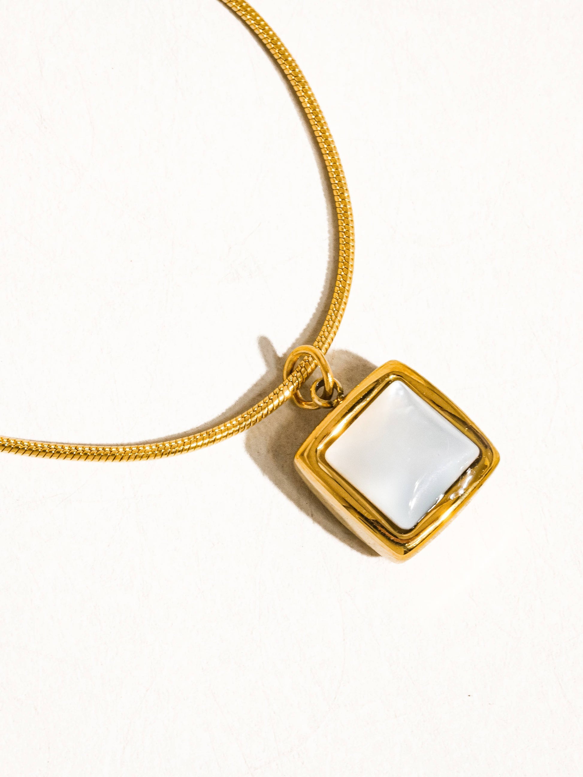 Gold pendant necklace with a square white inlay, elegant design perfect for any occasion.