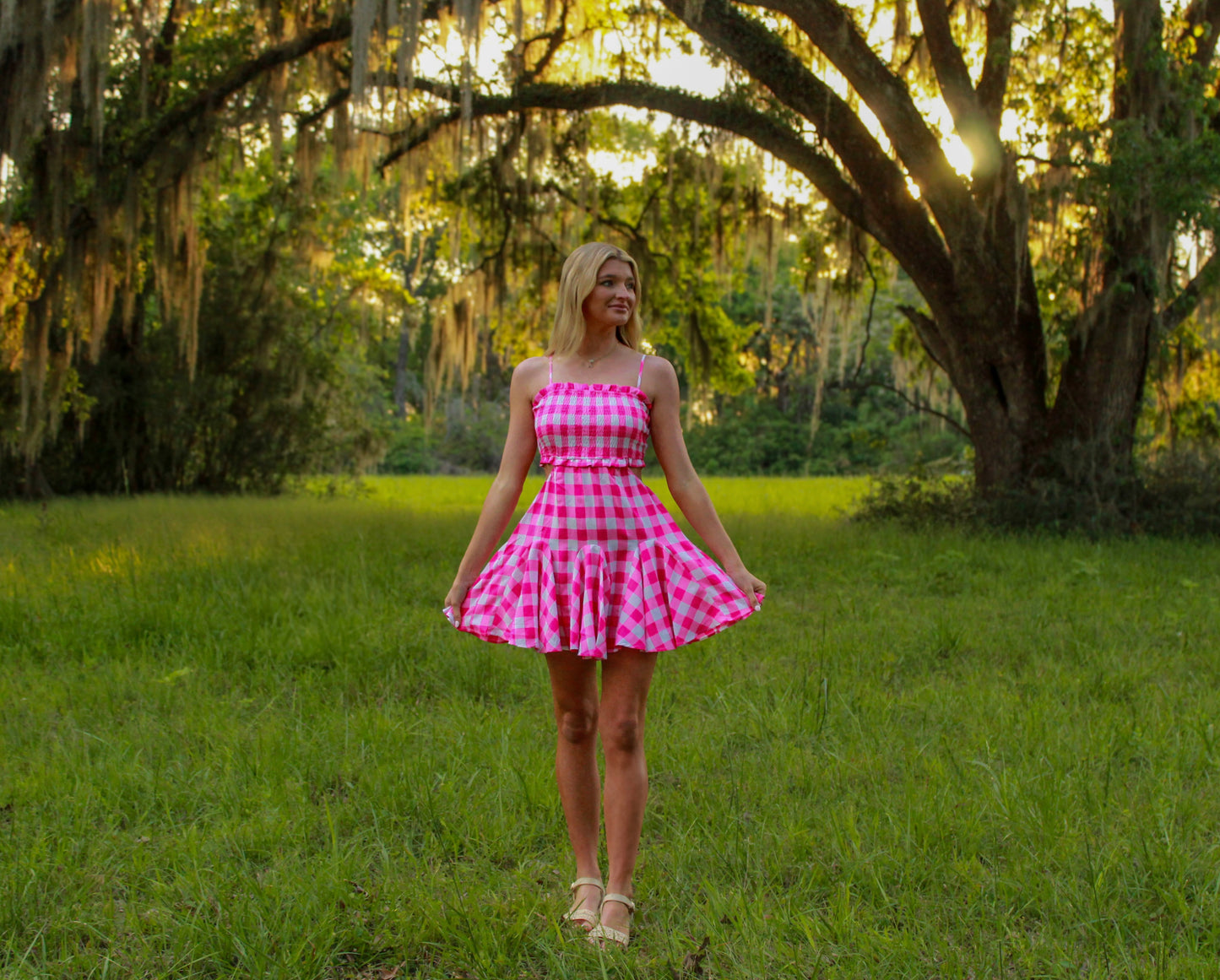 Model in a pink checkered dress, lightweight fabric, perfect for summer outings in a lush green setting.