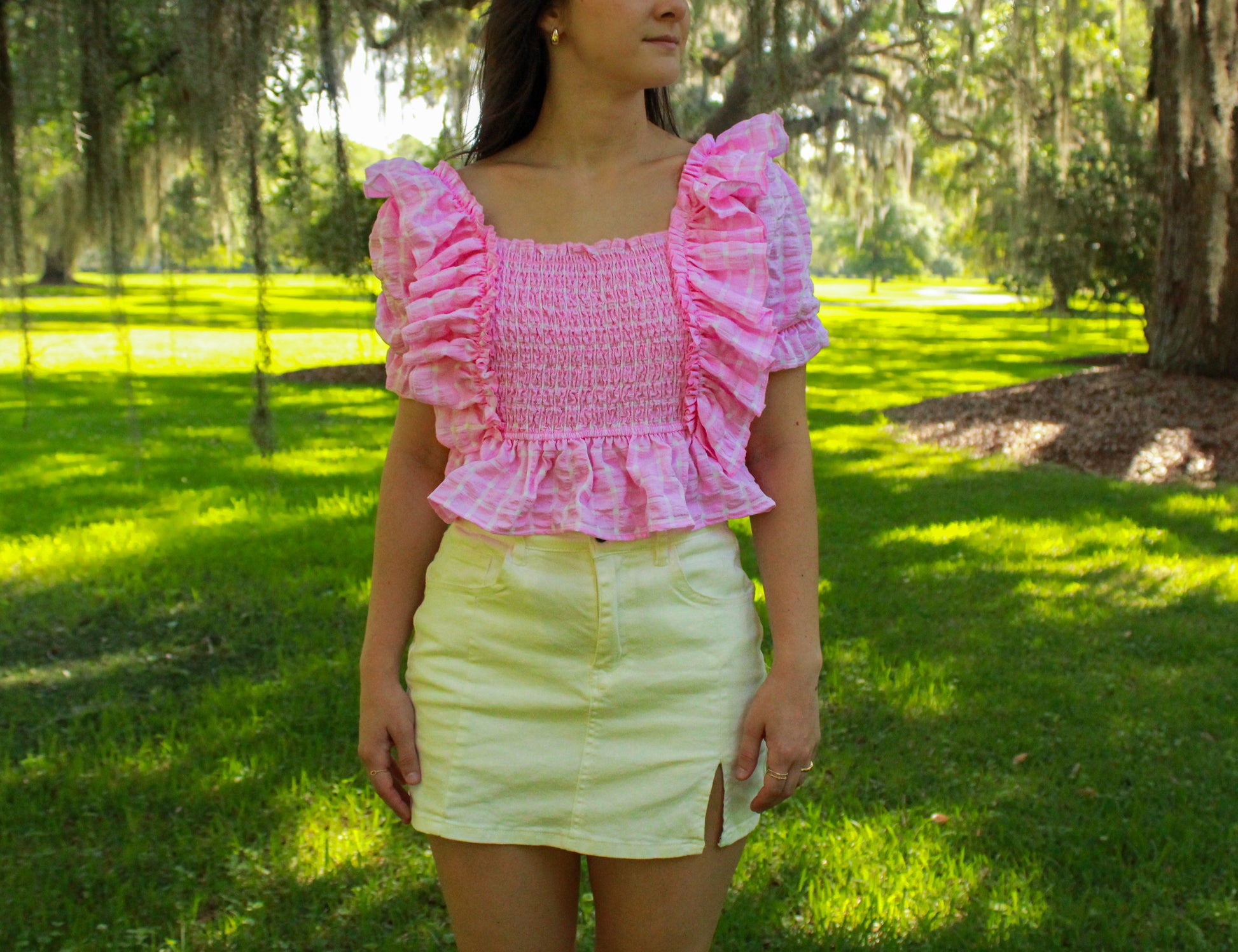 Pink smocked top with ruffled sleeves, paired with a white mini skirt in a sunny outdoor setting.