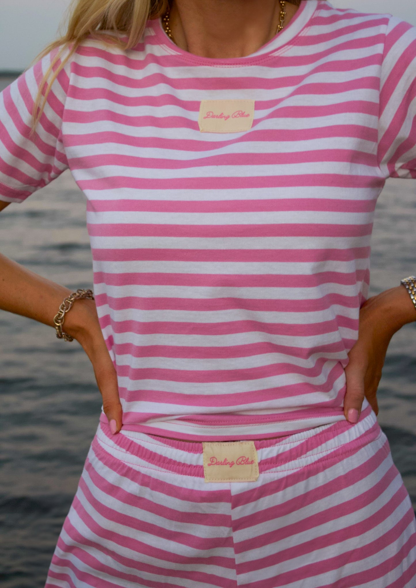 Person wearing a pink and white striped outfit with a visible brand label, standing by water.
