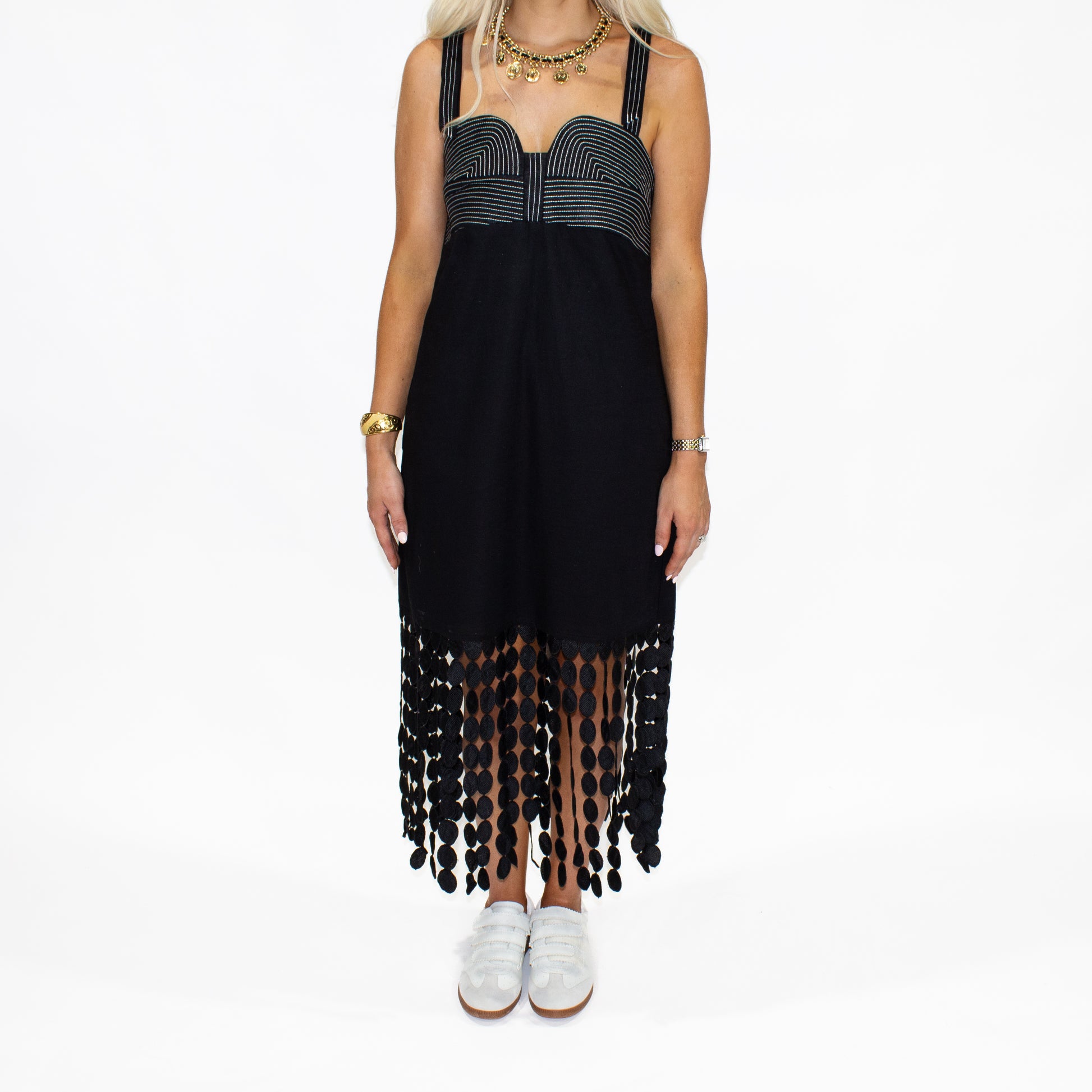 Black dress with fringe details worn by a person on a white background