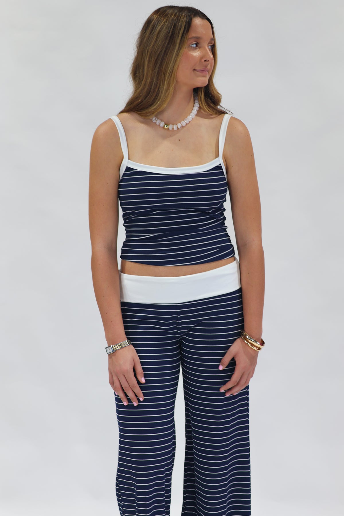 A woman modeling a matching two-piece loungewear set consisting of a navy blue and white striped camisole top and wide-leg pants, set against a plain light gray background.