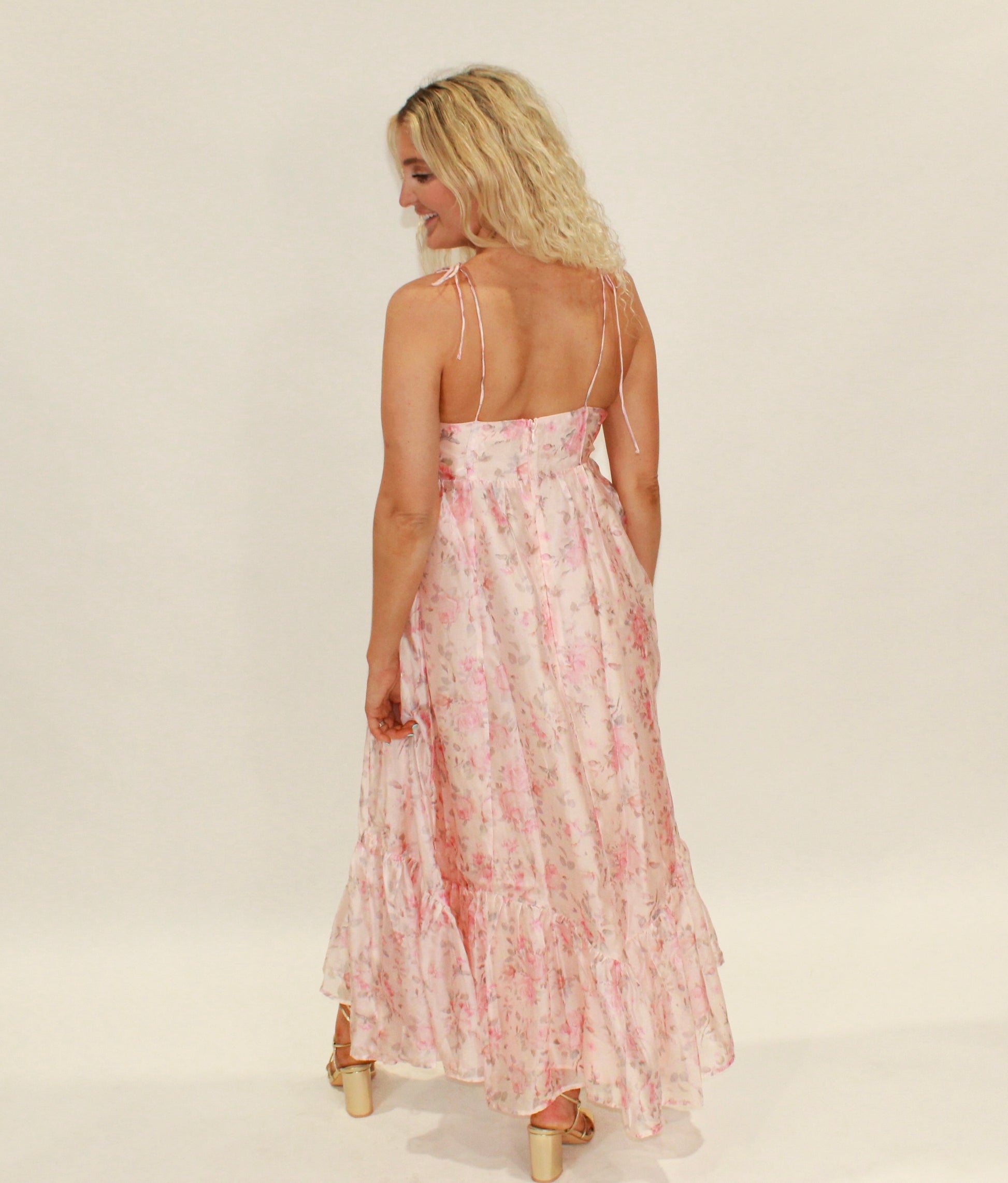 Back view of a flowy pink floral maxi dress with adjustable straps and ruffled hem.