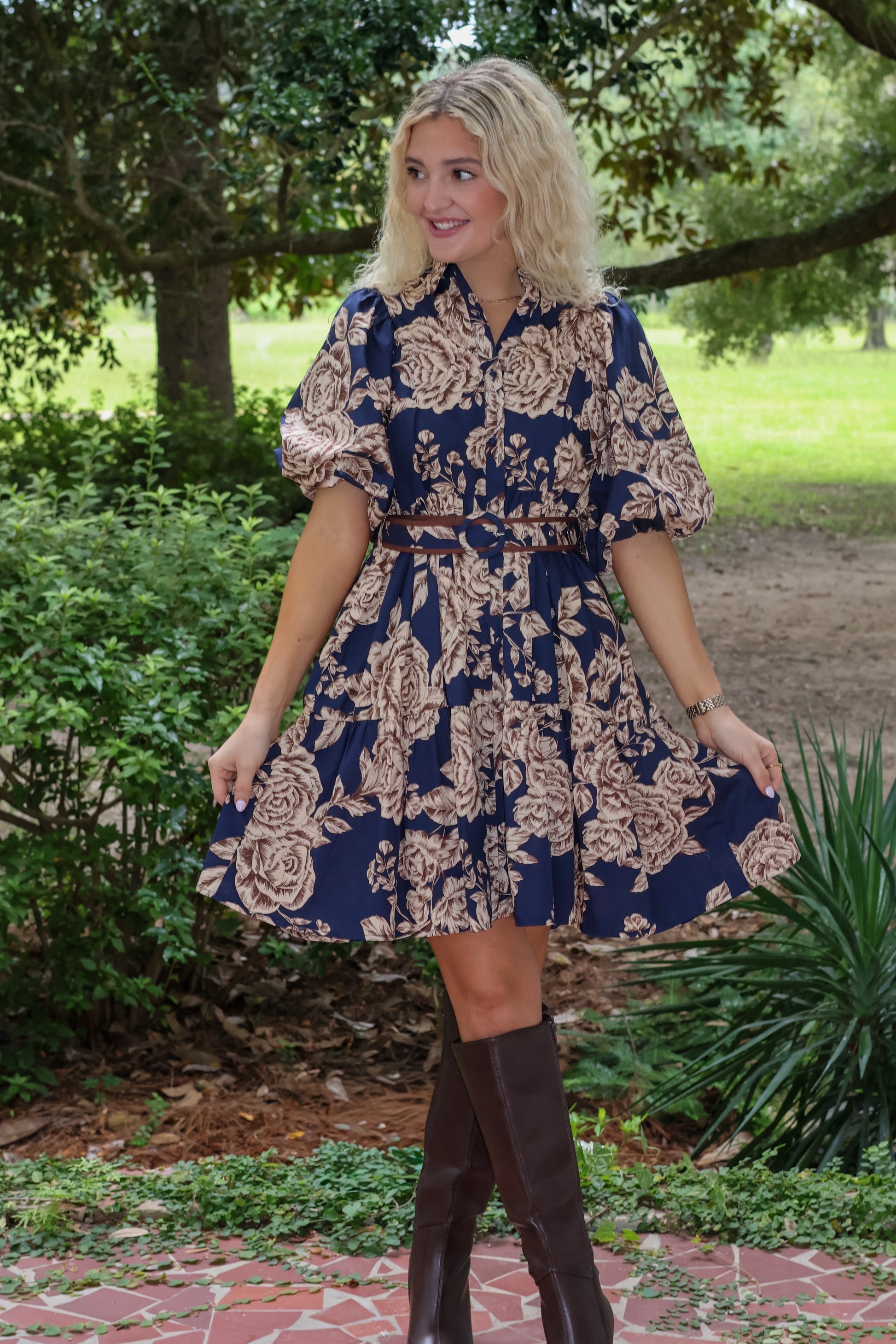 Woman wearing a floral dress with knee-high boots in a park setting