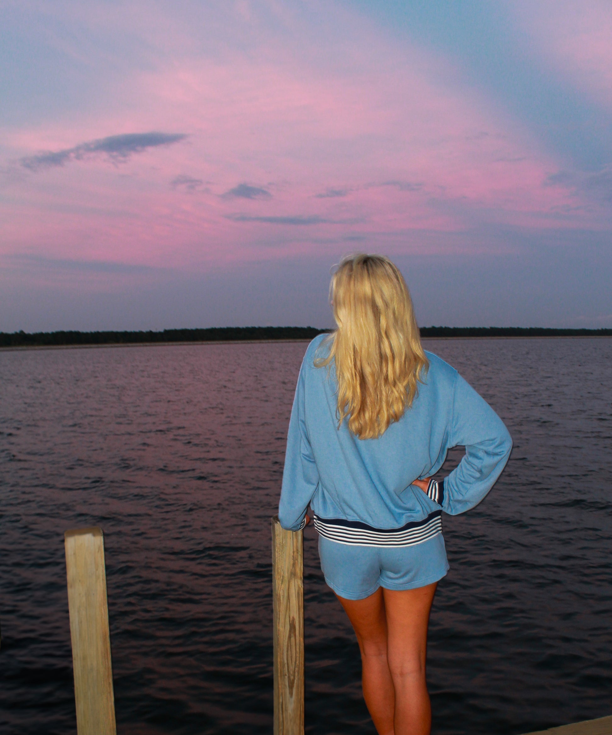 Person standing on a dock overlooking a body of water at sunset.
