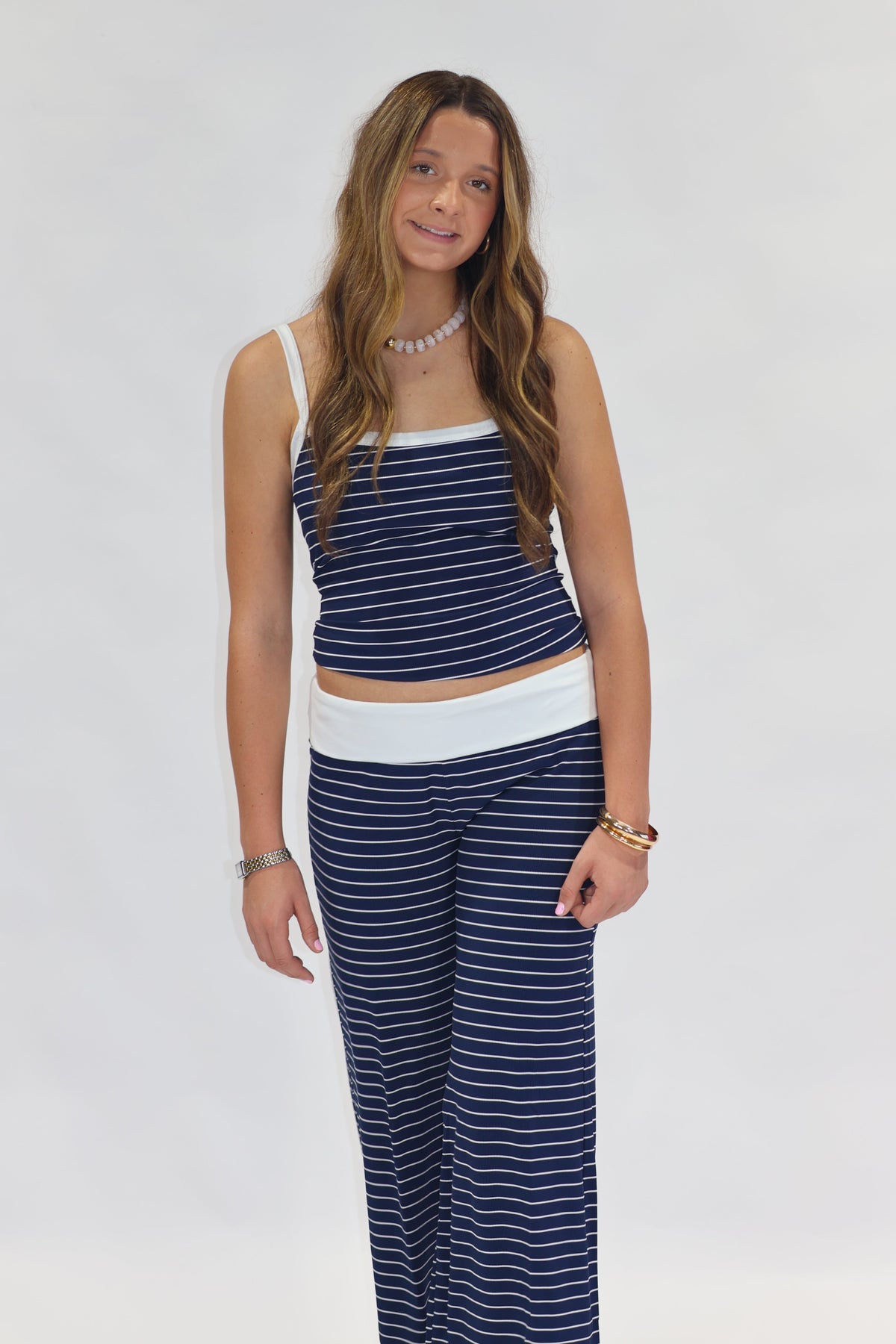 A woman modeling a matching two-piece loungewear set consisting of a navy blue and white striped crop top and wide-leg pants, set against a plain white studio background.
