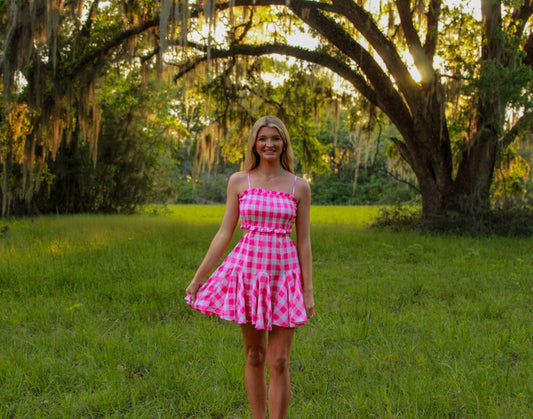 Pink gingham dress with smocked bodice, flowy skirt, perfect for summer outings in a scenic outdoor setting.