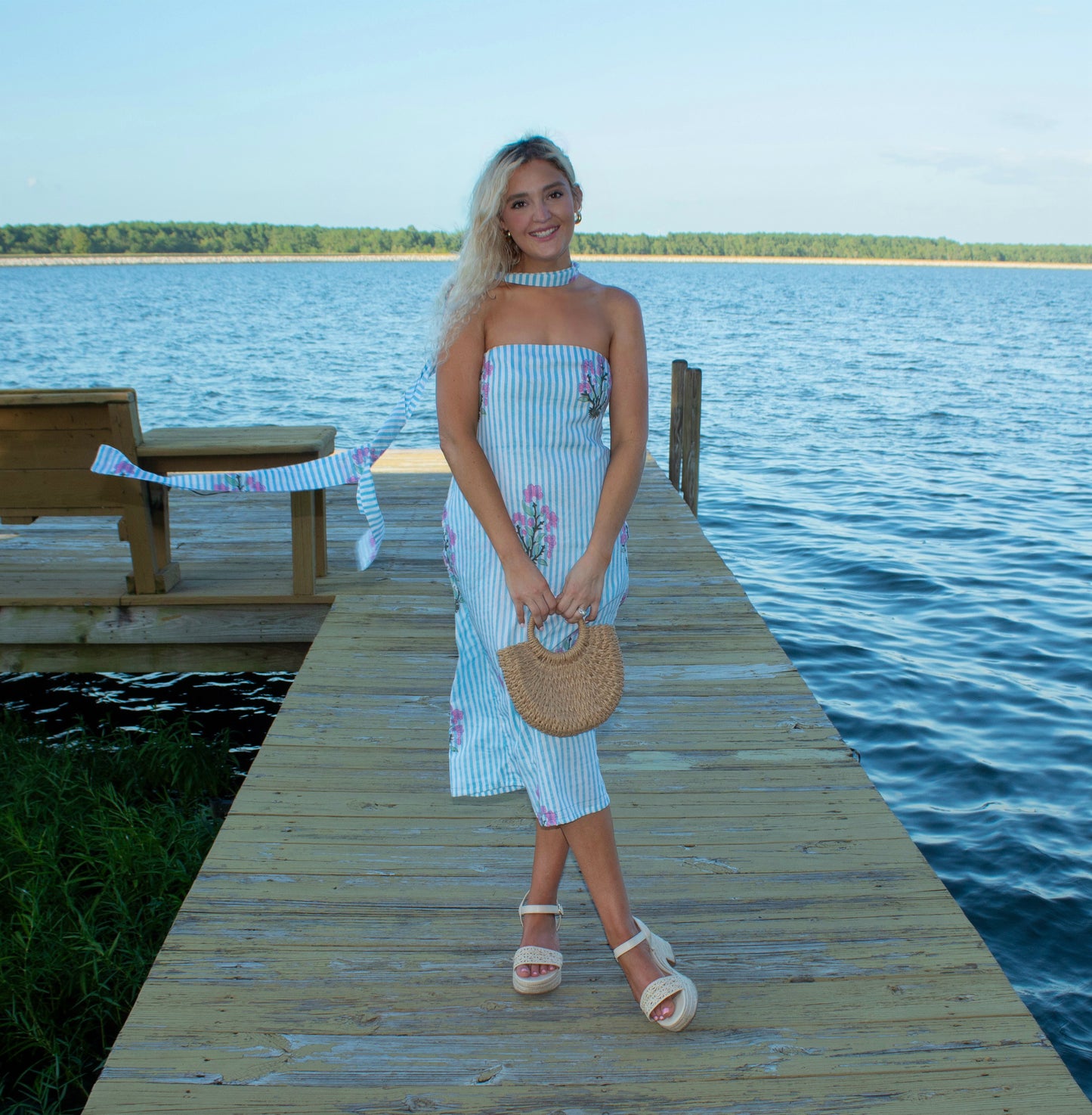 Woman in a striped dress standing on a dock by a lake