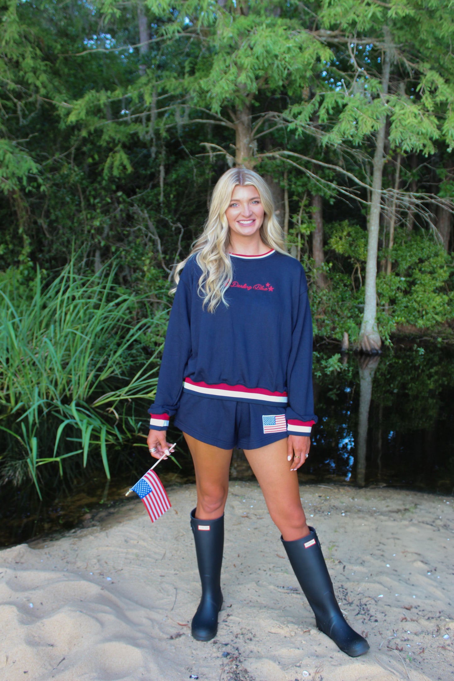 Navy blue pullover sweatshirt and shorts set with patriotic accents, model holding mini American flag.