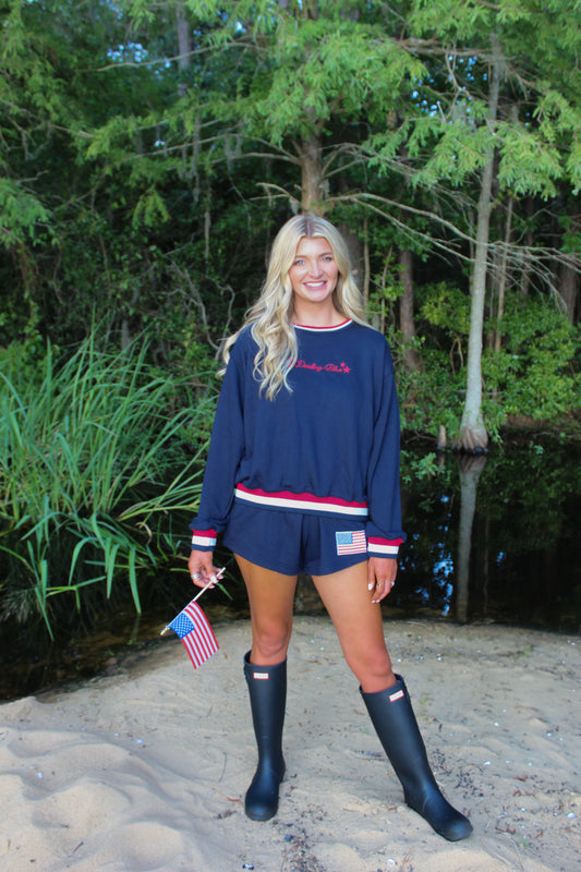 Navy blue pullover sweatshirt and shorts set with patriotic accents, model holding mini American flag.