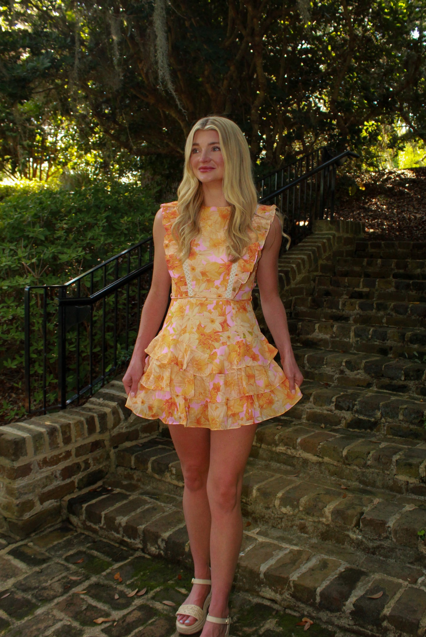 Floral ruffled dress in pastel orange and pink, perfect for summer occasions, made from lightweight fabric.