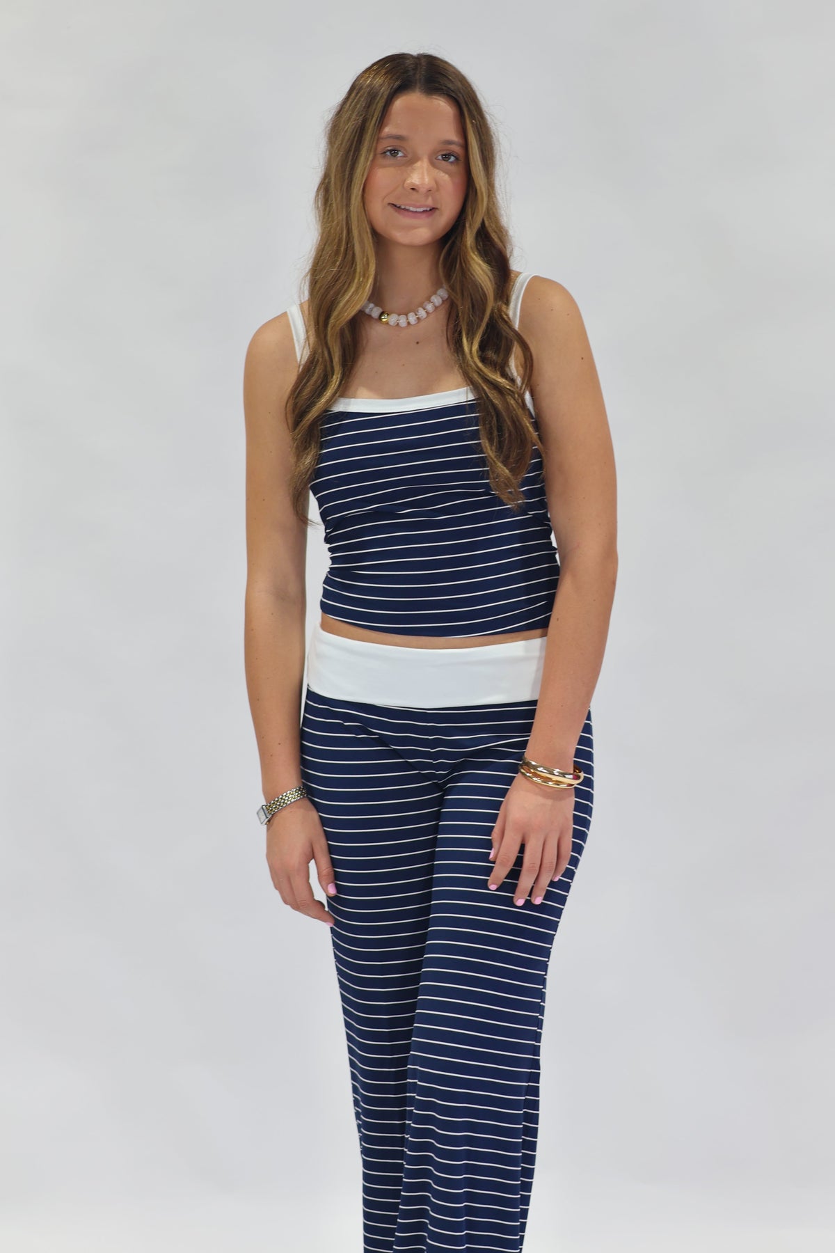 A woman modeling a matching two-piece loungewear set consisting of a navy blue and white striped crop top and wide-leg pants, photographed against a neutral light gray studio background.