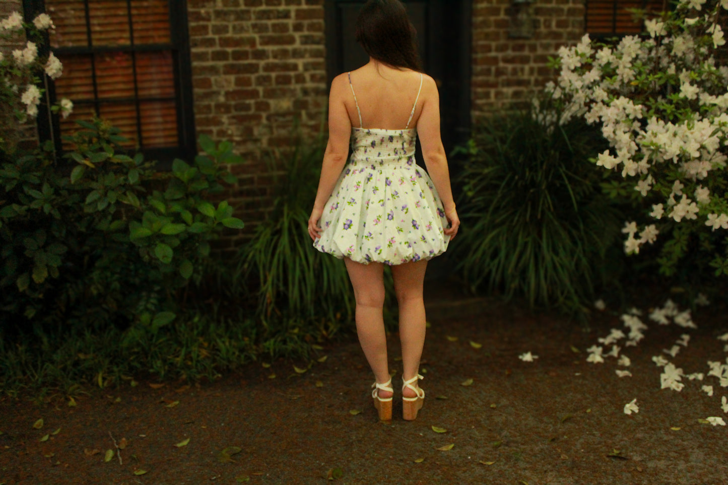 Back view of a white floral summer dress with adjustable straps and puffed skirt, paired with sandals.