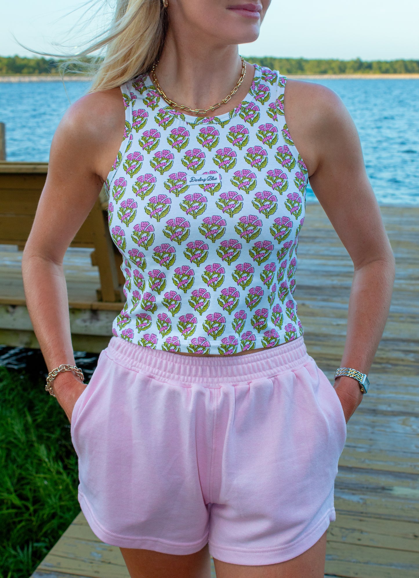 Woman wearing a patterned top and pink shorts by a waterfront.