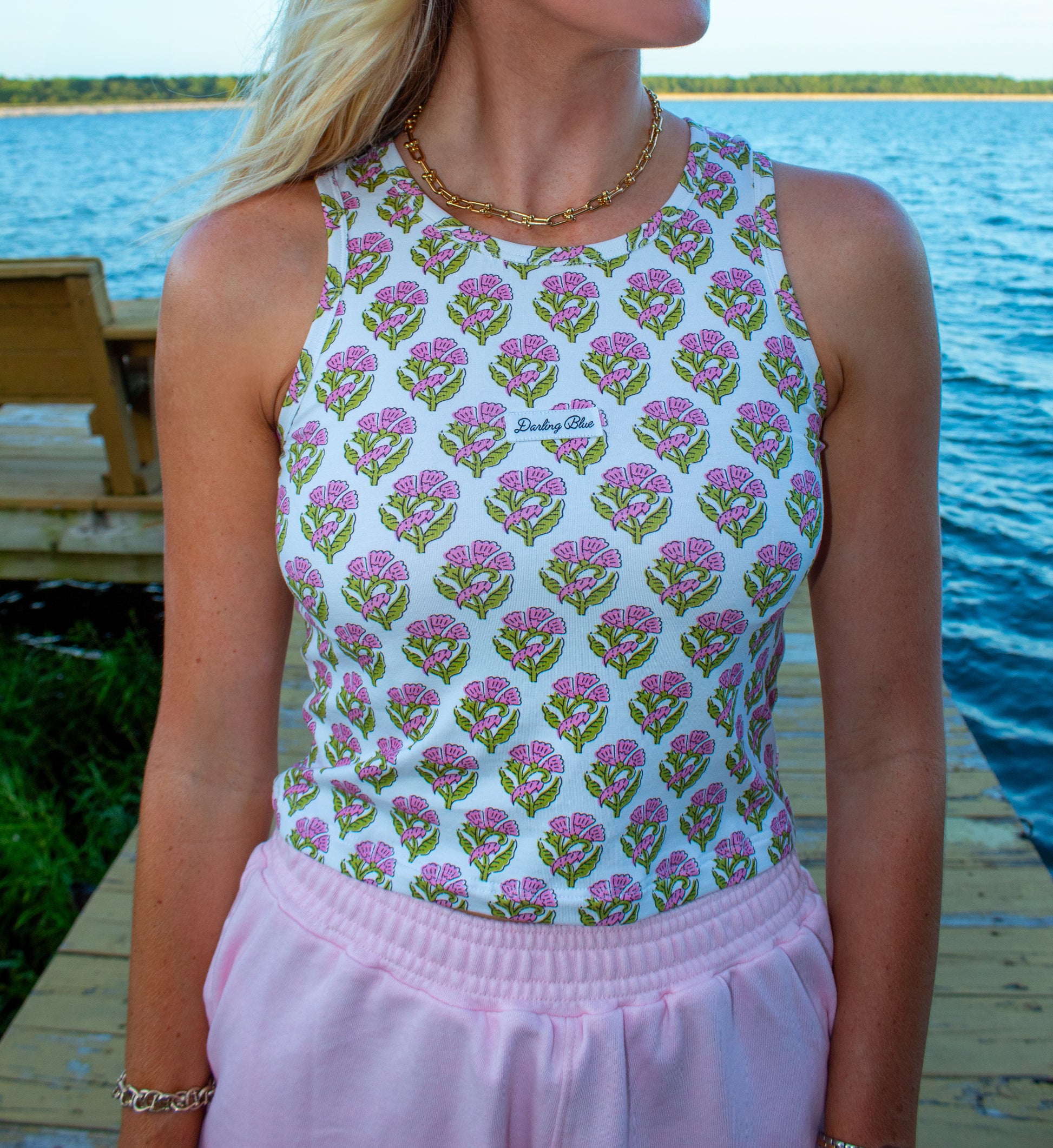 Woman wearing a sleeveless floral top and pink pants by a lakeside.
