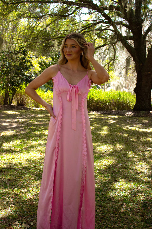 Elegant pink satin maxi dress with ruffle details and a bow, perfect for summer outings.