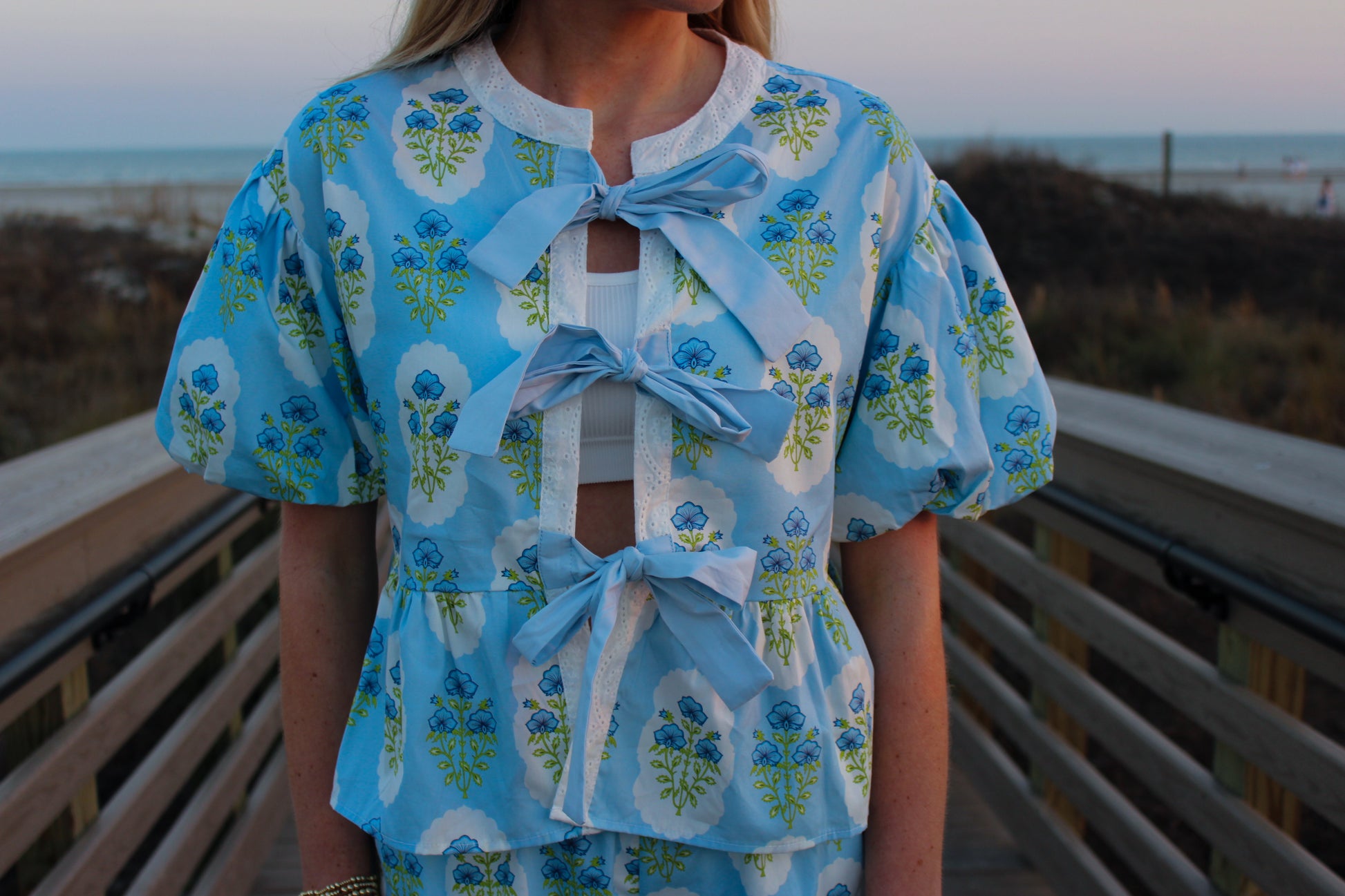 Floral blue blouse with puff sleeves and bows, perfect for summer wear, made from lightweight fabric.