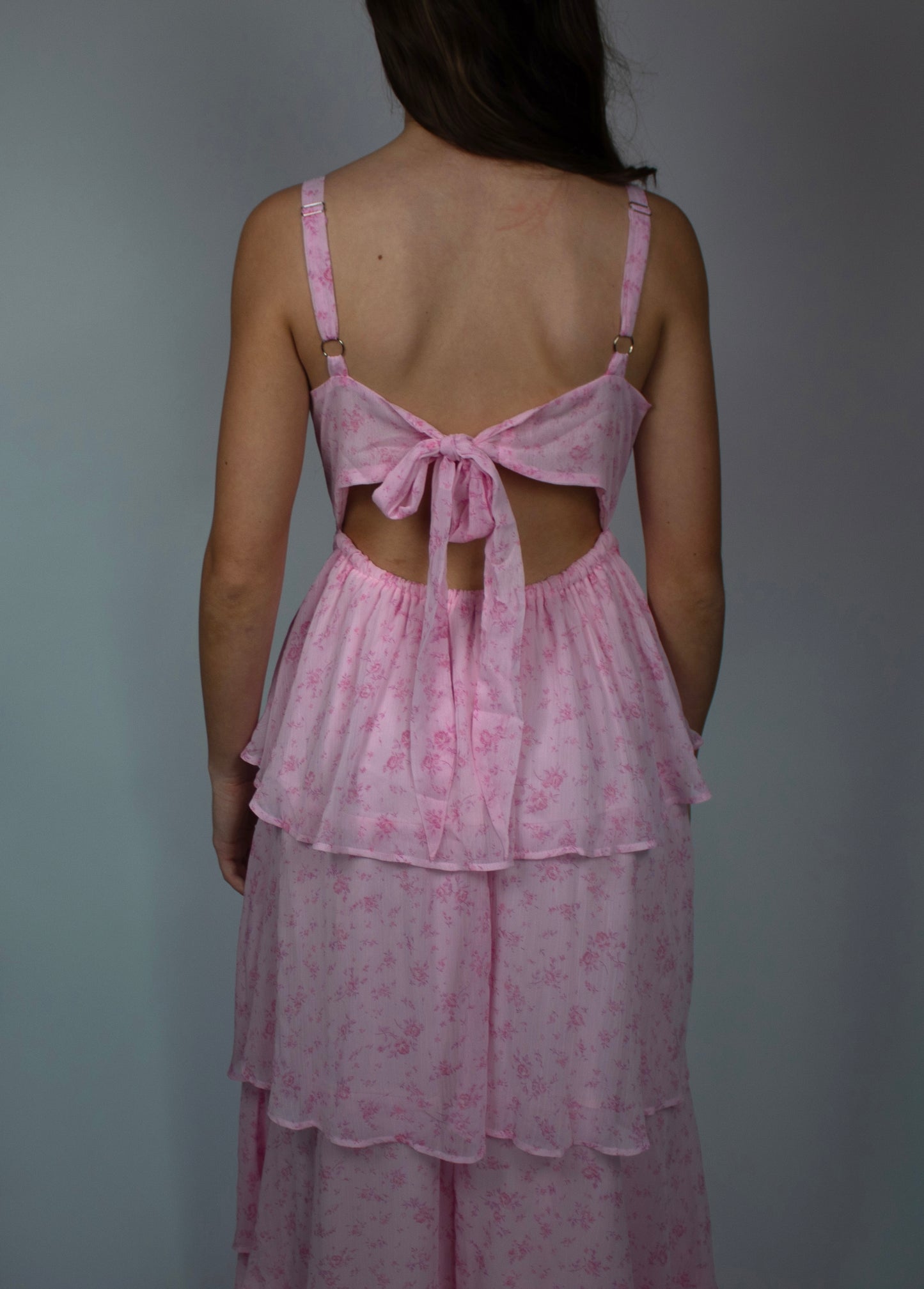 Back view of a pink floral tiered dress with adjustable straps and tie detail.