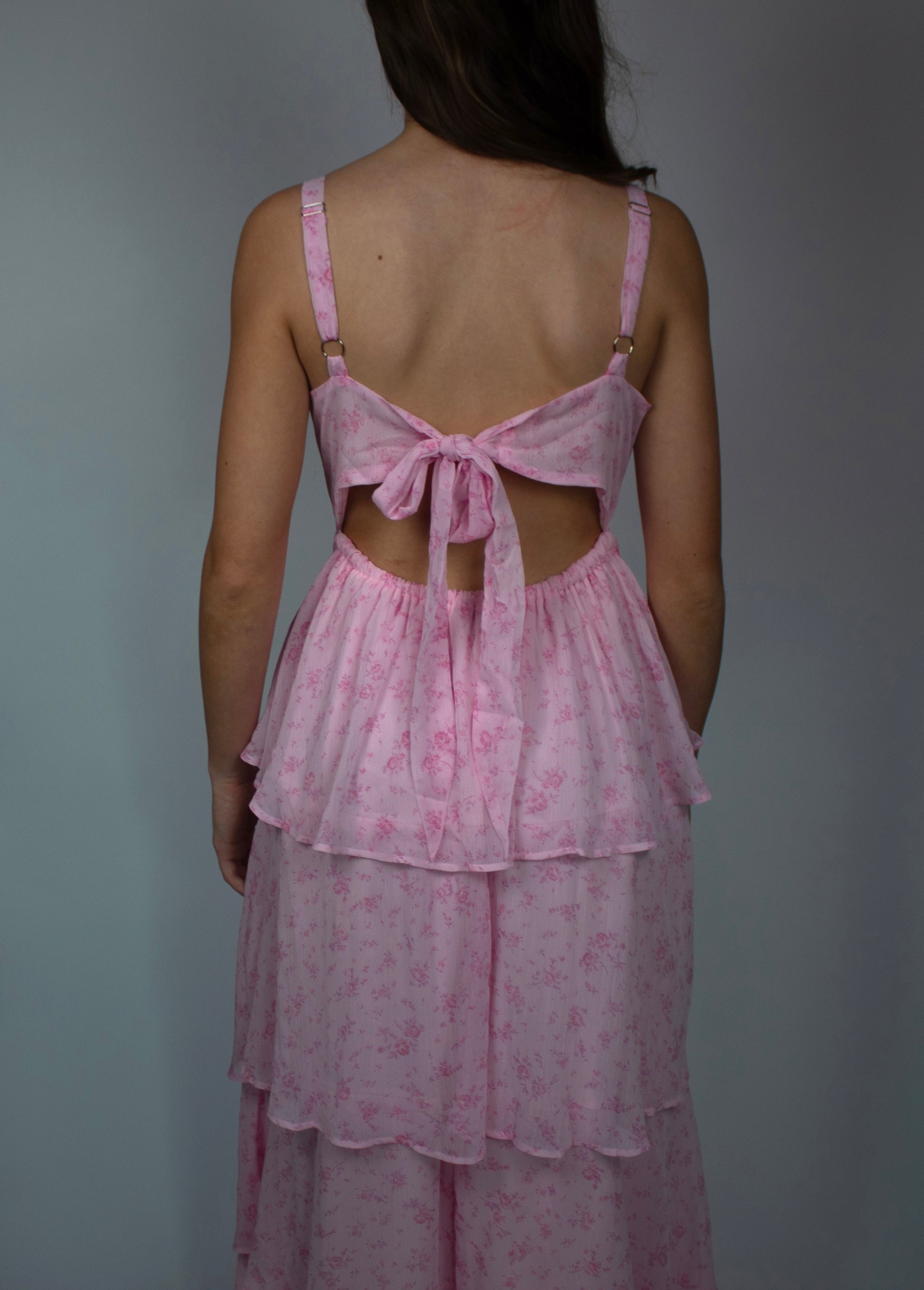 Back view of a pink floral tiered dress with adjustable straps and tie detail.