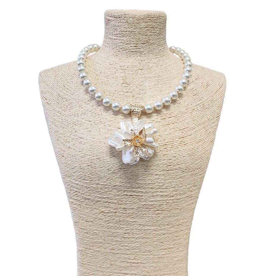 Pearl necklace with a floral pendant on a mannequin bust.